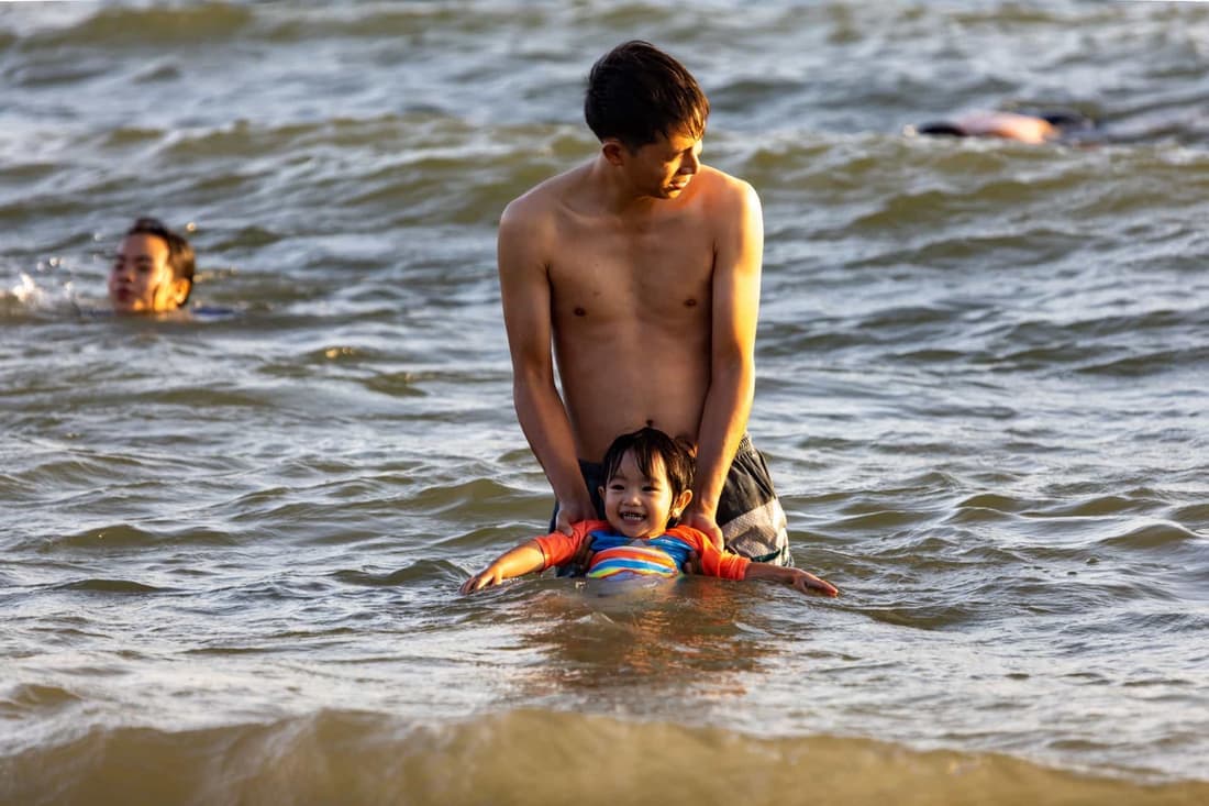 Father guides his son in the shallow sea waves, enjoying a sunny summer day on the beach