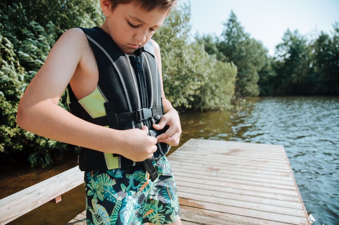 A boy fastening a life jacket on a sunny day at a lakeside jetty, ready for water sports