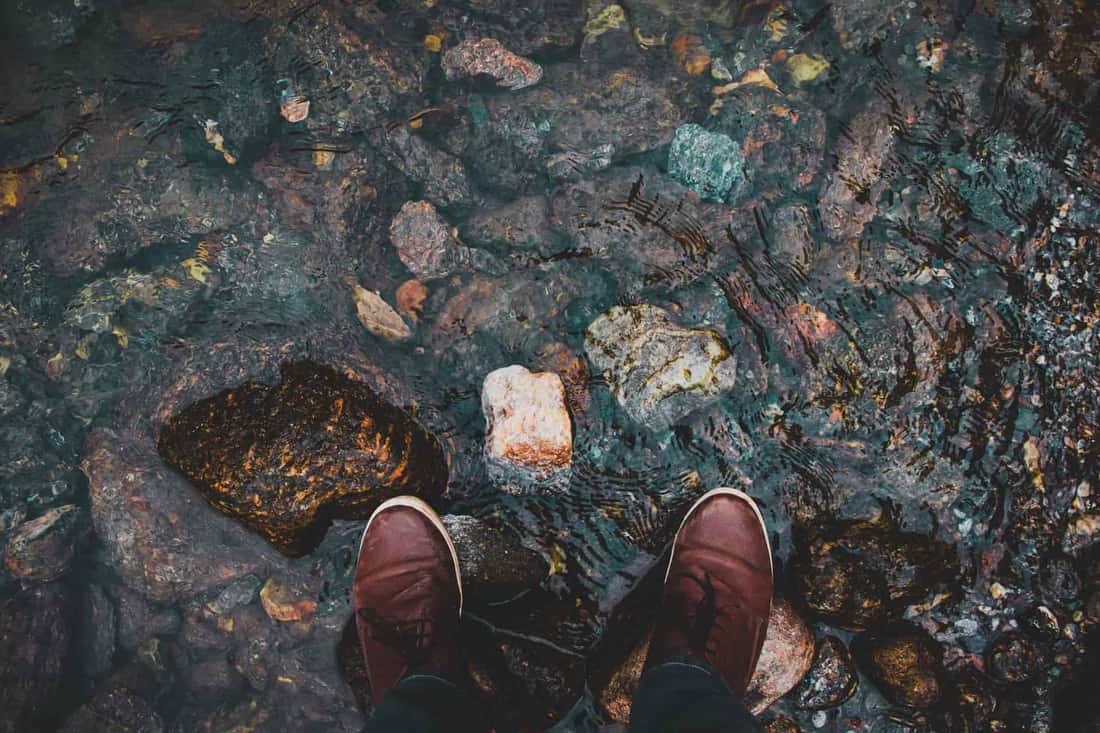 Top-down view of brown shoes in a clear rocky stream