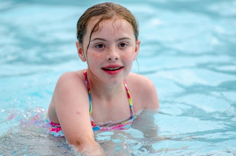 A young girl with freckles having fun swimming in a clear blue pool
