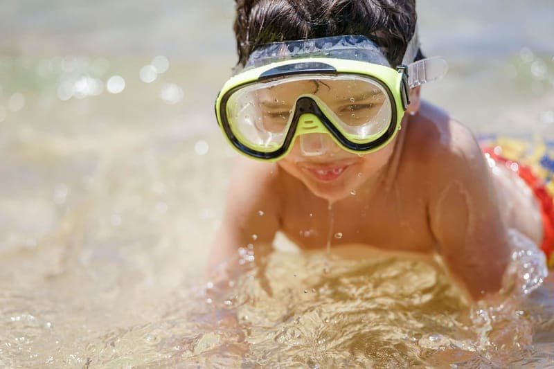 A smiling child wearing goggles enjoys swimming on a sunny summer day
