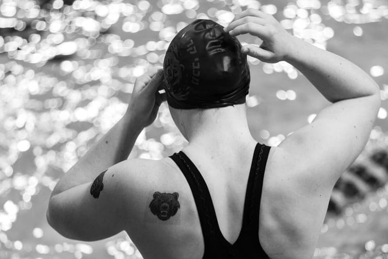 Black and white image of a swimmer adjusting their cap at an indoor pool